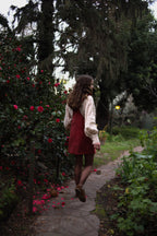 Modelo usando jardinera vestido corto de cotelé color burdeo, caminando por un sendero