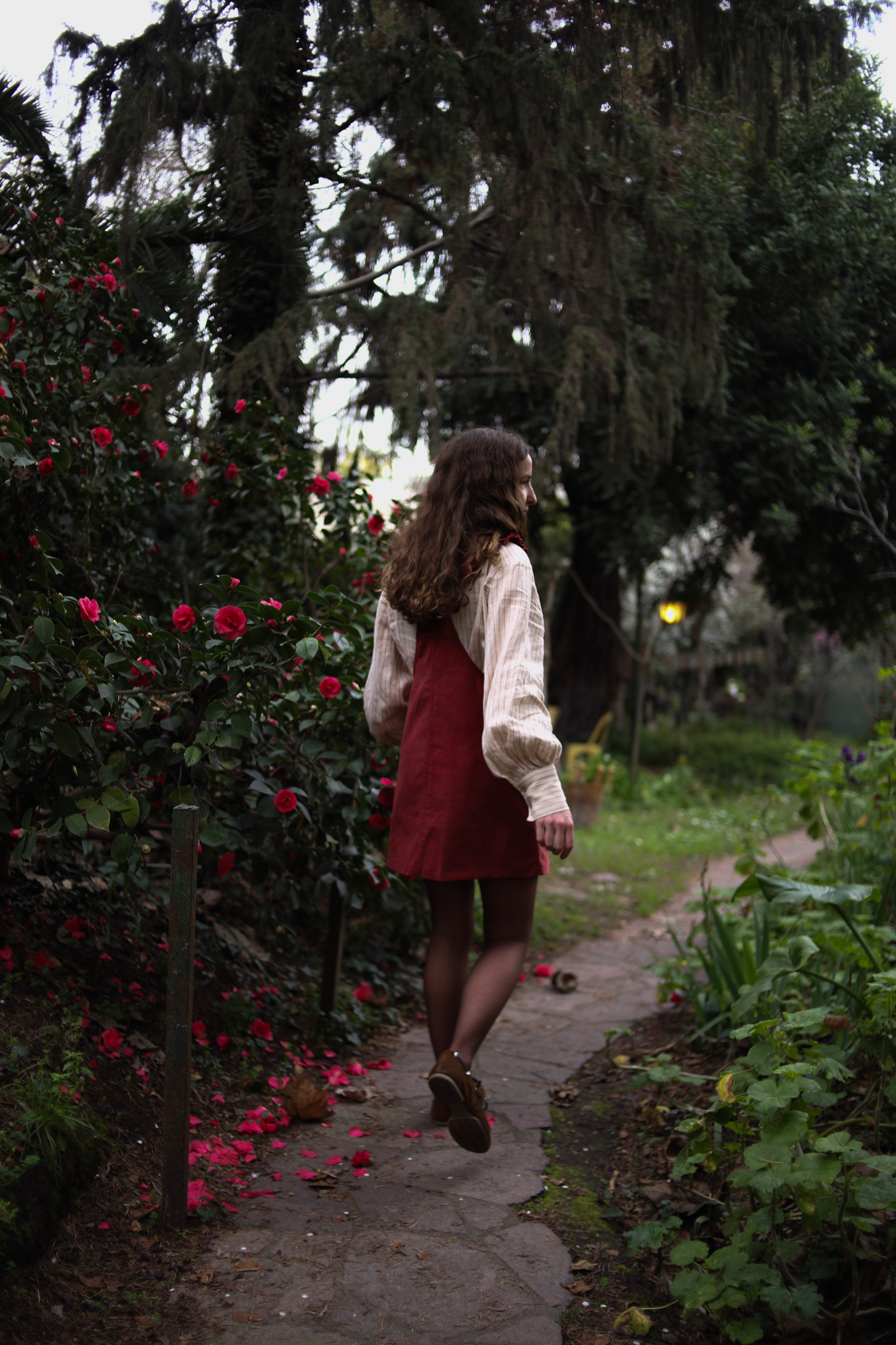 Modelo usando jardinera vestido corto de cotelé color burdeo, caminando por un sendero